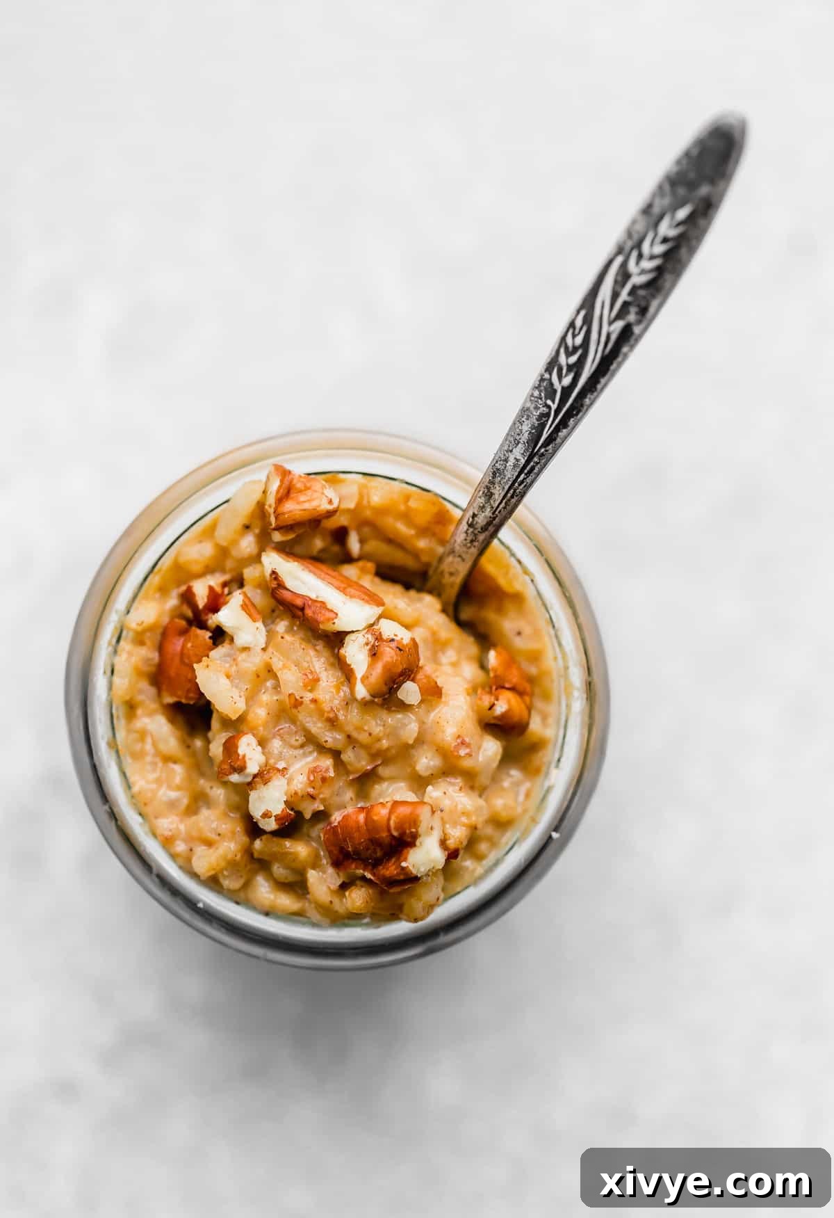 Spiced Pumpkin Rice Pudding 11 Overhead photo of Pumpkin Rice Pudding in a glass jar that is topped with chopped pecans, highlighting its inviting presentation.