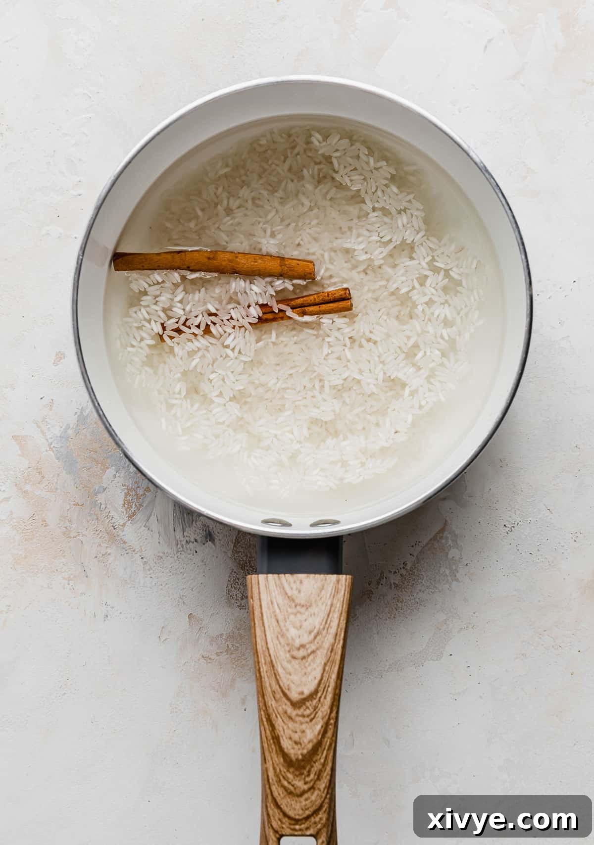 Spiced Pumpkin Rice Pudding 4 A saucepan with water, rice, and two cinnamon sticks in it, just beginning to simmer.
