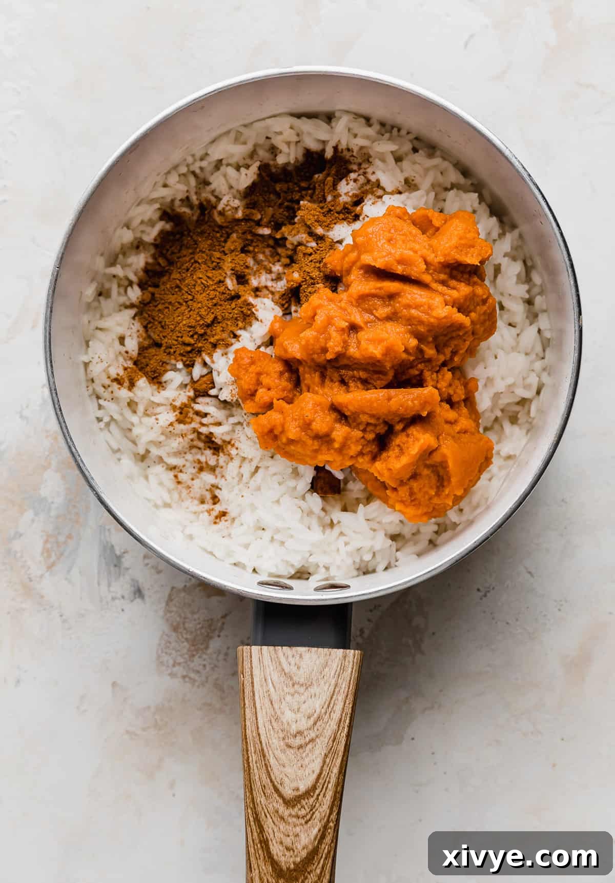Spiced Pumpkin Rice Pudding 6 Pumpkin puree and fall spices being added overtop cooked rice and milk in a saucepan.