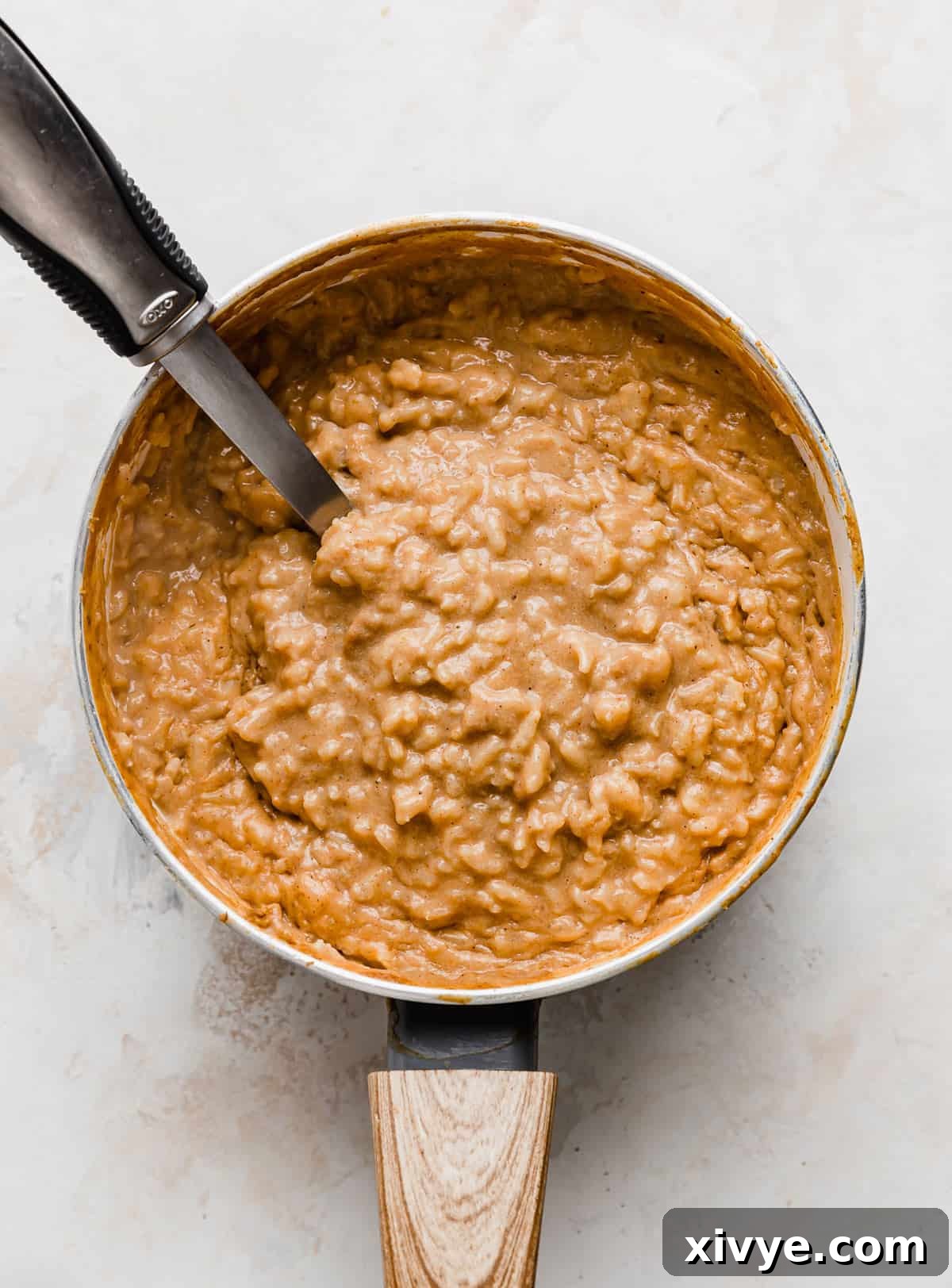 Spiced Pumpkin Rice Pudding 10 Pumpkin Rice Pudding in a saucepan on a textured white background, showcasing its inviting texture.