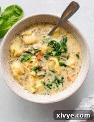 Hearty Italian Sausage Tortellini Soup 8 A white bowl with Creamy Sausage Tortellini and Spinach soup in it, on a white background.