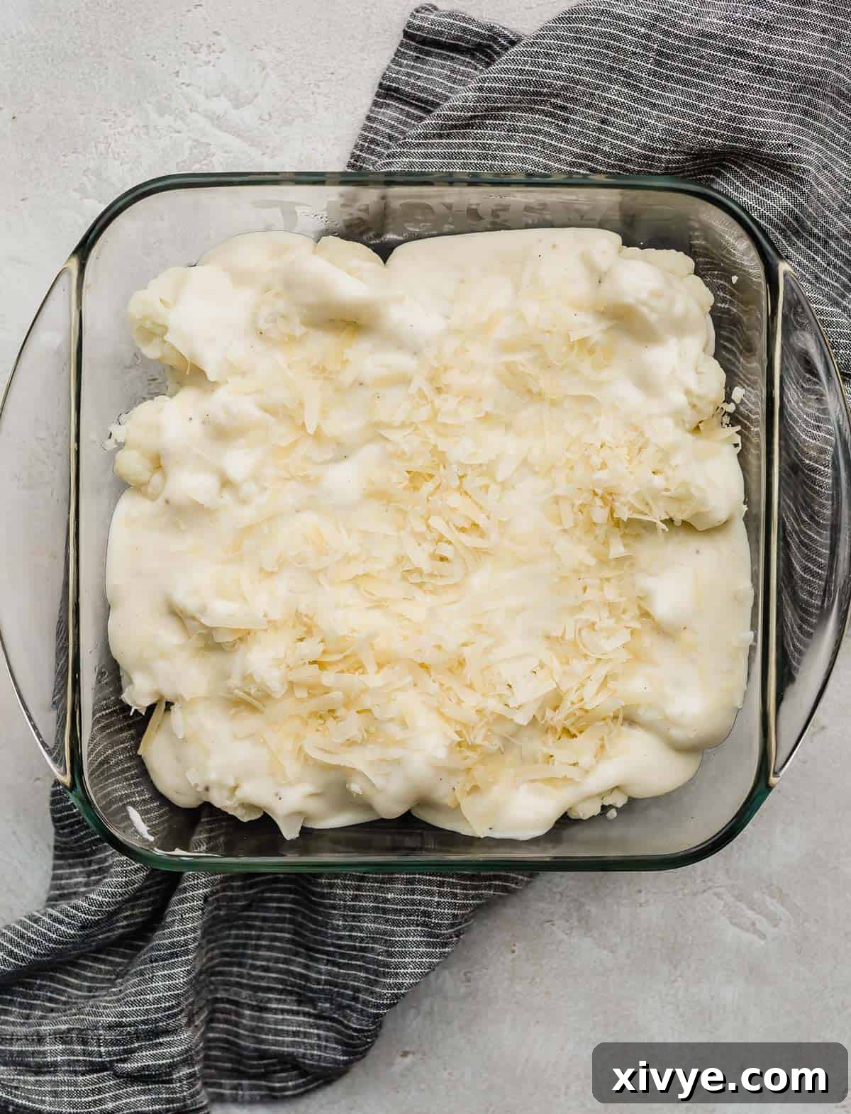Unbaked Cauliflower Gratin topped with gruyere cheese in a square casserole dish.