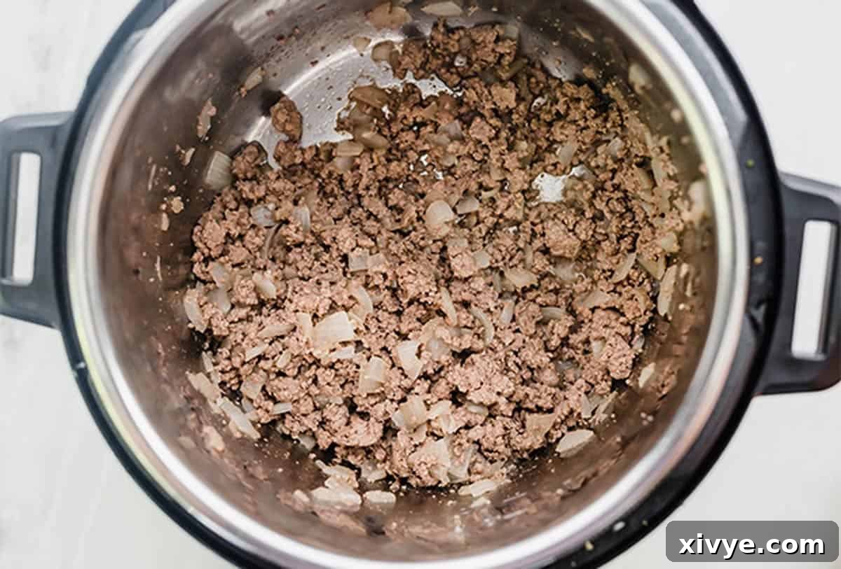 Ground beef and diced onions being sautéed in an Instant Pot, a key step for flavorful Instant Pot Beef Stroganoff.