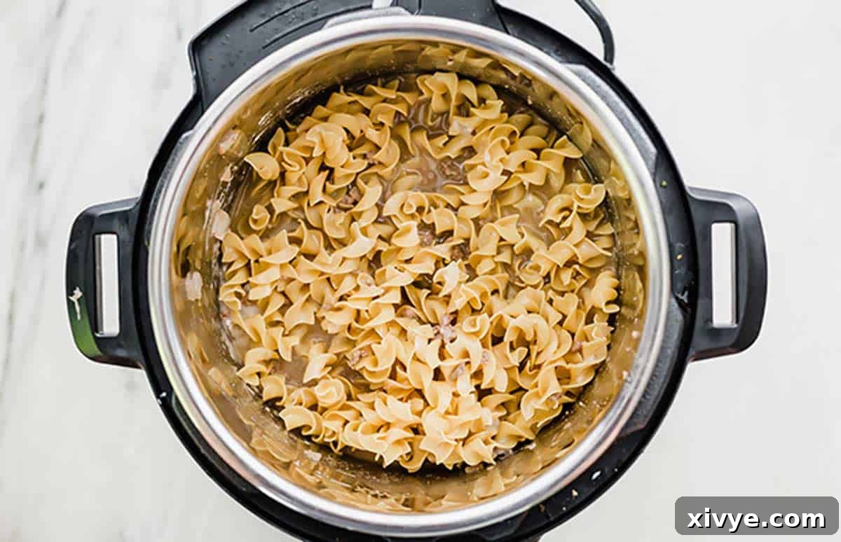 Egg noodles cooking in an Instant Pot with other ingredients, showing the one-pot convenience of Instant Pot Beef Stroganoff.
