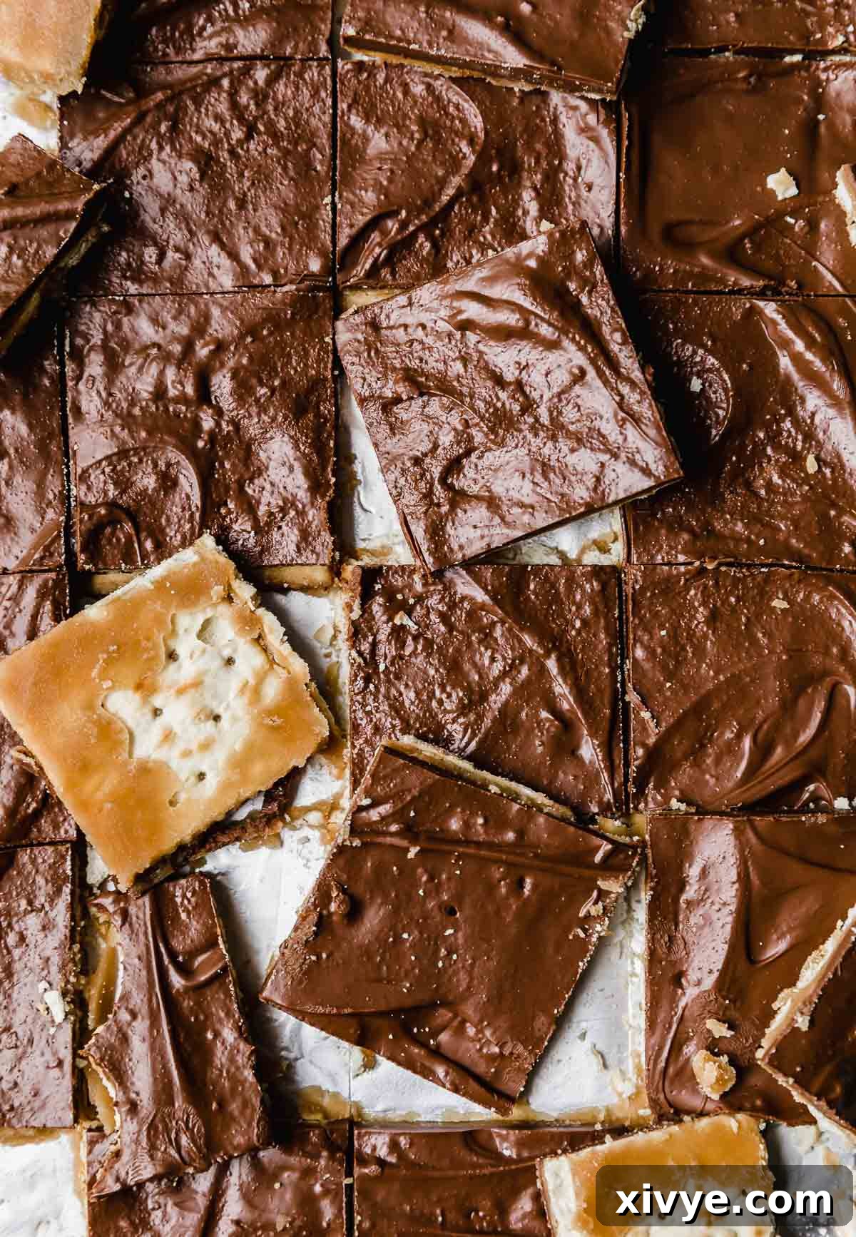 An inviting overhead photo of a large batch of Christmas Crack, meticulously cut into uniform squares, arranged beautifully on tan parchment paper, highlighting the contrasting layers of chocolate, toffee, and cracker. The pieces are ready to be served or packaged for holiday gifting.