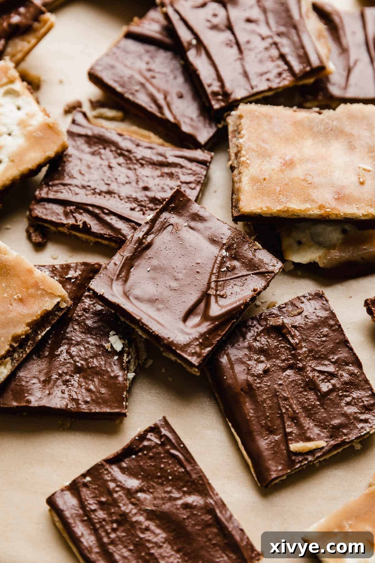 Delicious Christmas Crack, perfectly cut into uniform squares, arranged beautifully on rustic Kraft parchment paper, highlighting its tempting layers of chocolate, toffee, and crisp cracker. The ideal holiday dessert ready for serving.