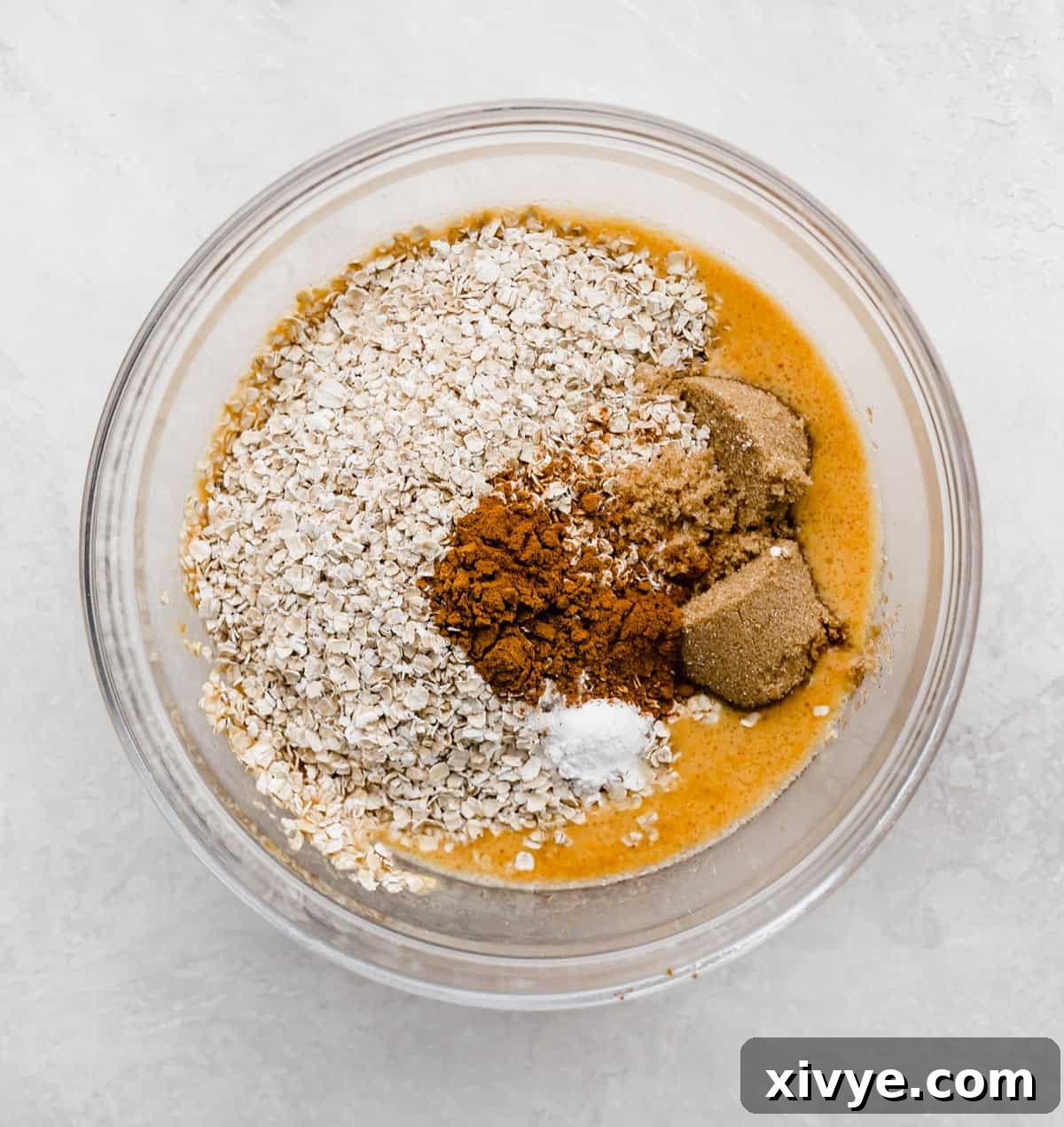 Spiced Pumpkin Oat Muffins 5 A glass bowl with oats, brown sugar, pumpkin puree, and baking powder in it, ready to be mixed into a smooth batter.