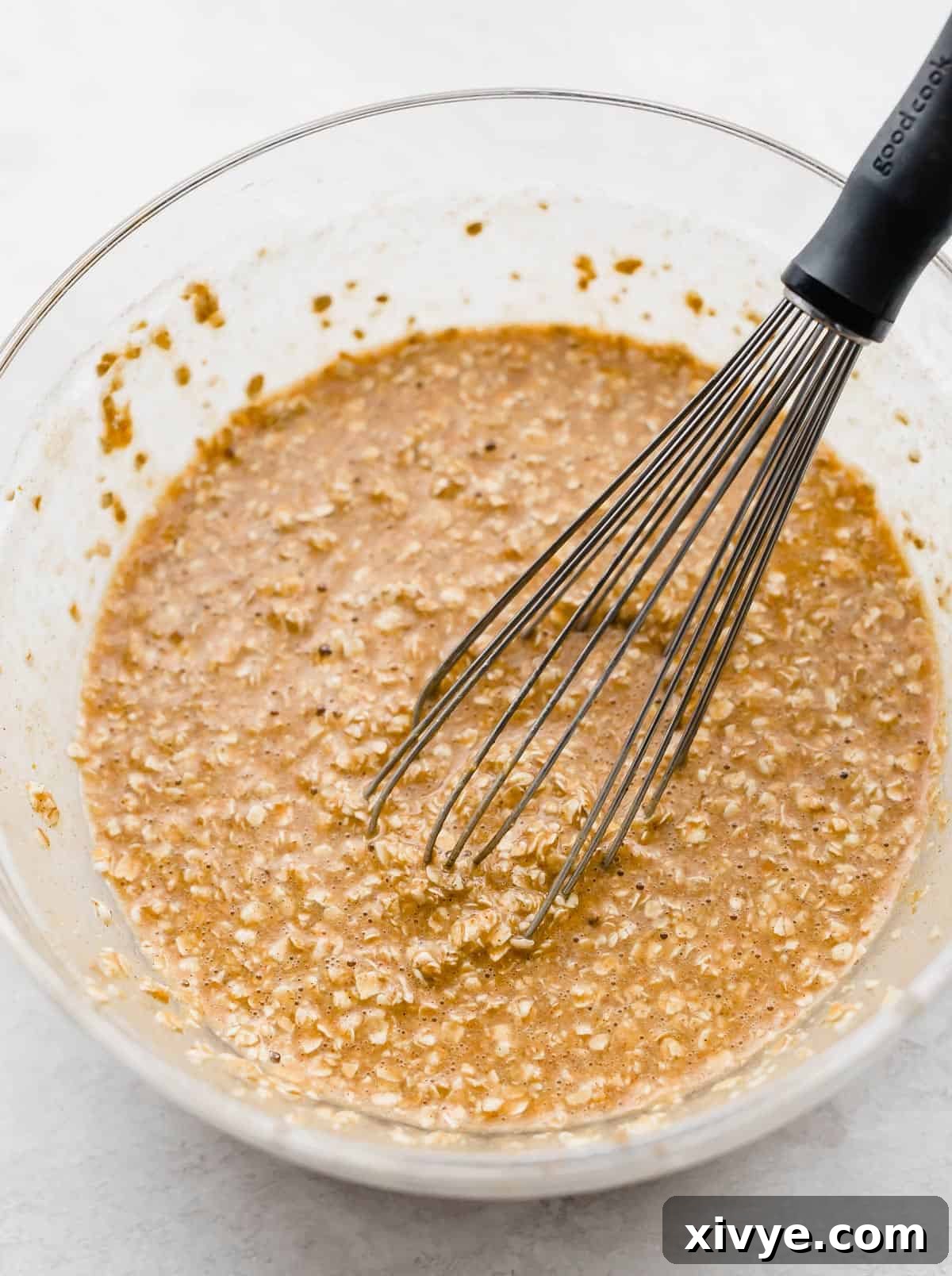 Spiced Pumpkin Oat Muffins 6 A whisk stirring Pumpkin Baked Oatmeal Cups batter in a glass bowl, showing the consistency before pouring.