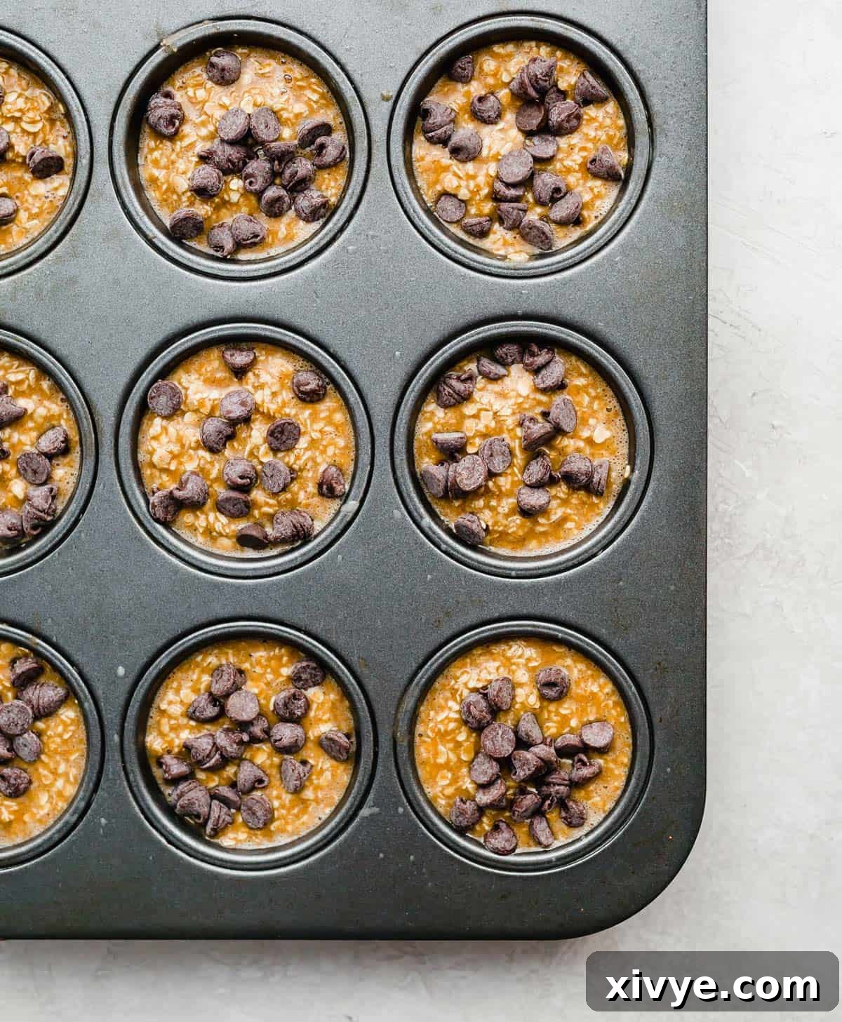 Spiced Pumpkin Oat Muffins 7 Pumpkin Baked Oatmeal Cups batter topped with chocolate chips in a muffin tin, ready to be baked to perfection.