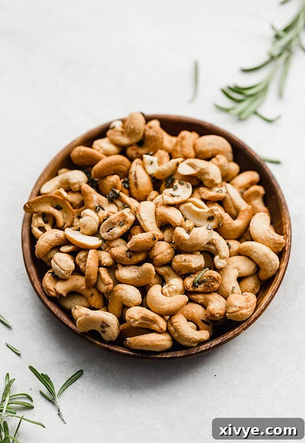 A plate of rosemary cashews surrounded by fresh rosemary sprigs, emphasizing the key herb.