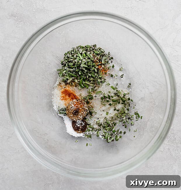 A glass bowl with fresh rosemary, cayenne, salt, and melted butter, ready to be mixed.