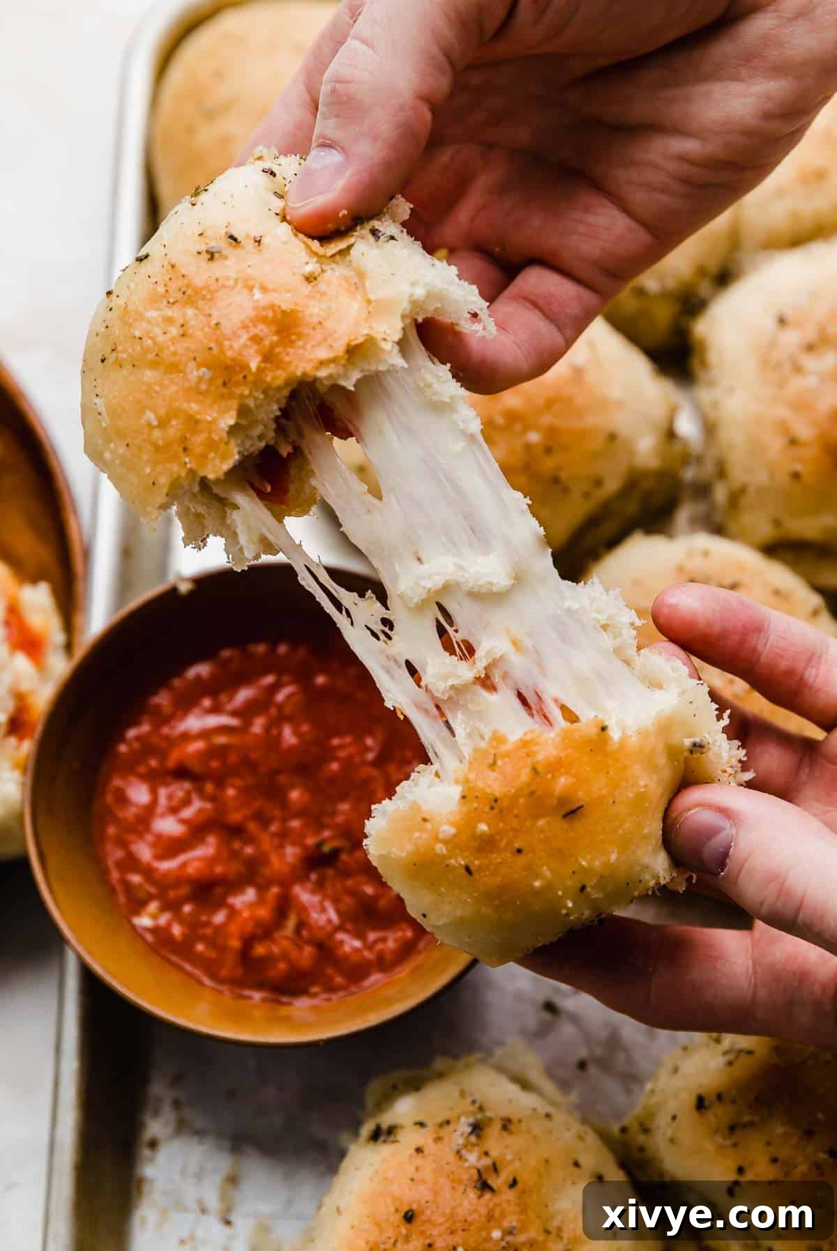 Two hands pulling a pizza roll apart showing the inside stretchy mozzarella cheese.