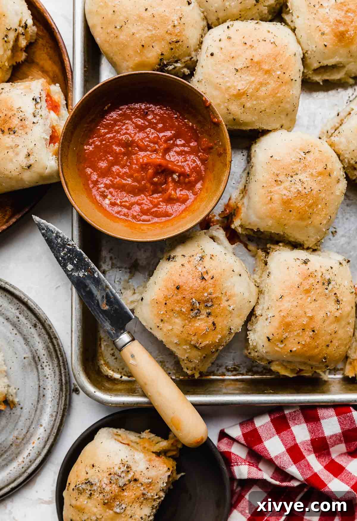 Overhead photo of a baking sheet topped with pizza rolls and a bowl of red dipping sauce.
