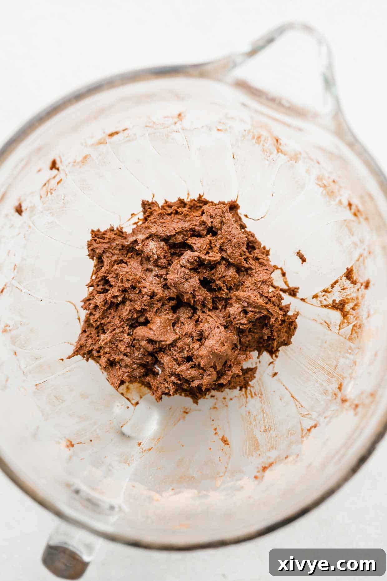 Brown chocolate turtle cookie dough in a glass mixing bowl on a white background.