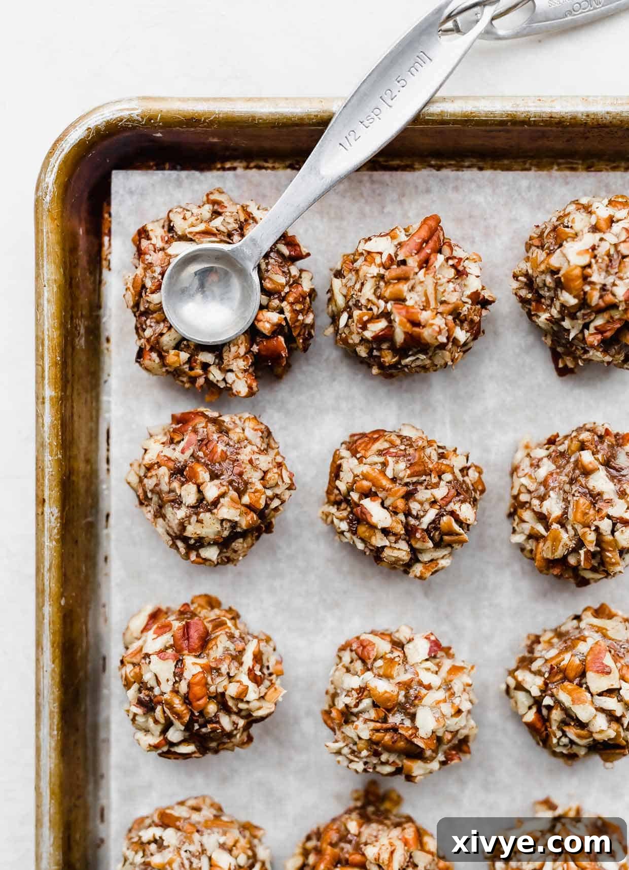 A metal teaspoon pressing into a pecan covered chocolate cookie dough ball (Turtle Cookies) to make an indent for the caramel to sit.