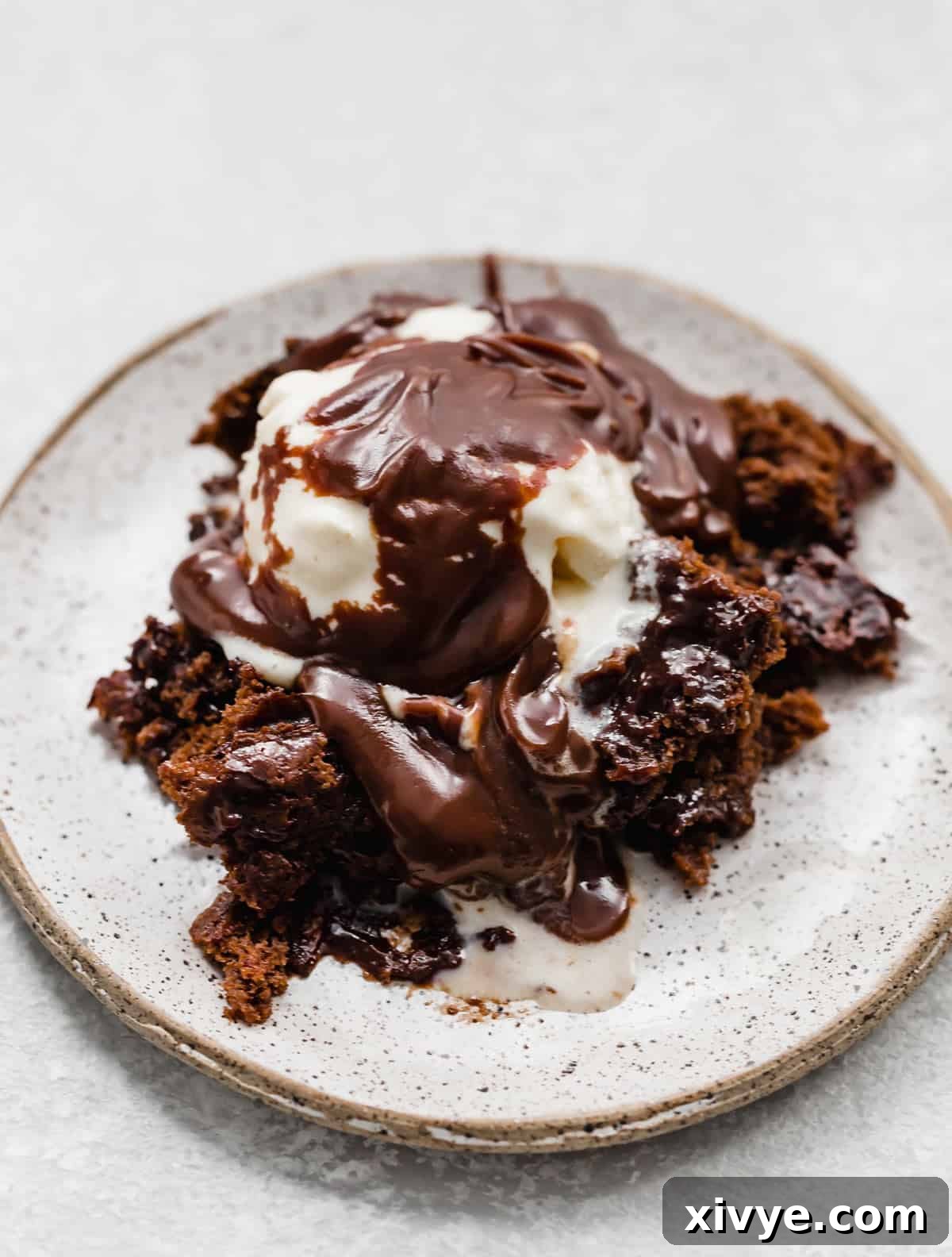 Molten Chocolate Dream 9 Hot Fudge Cake on a white plate with a scoop of ice cream and hot fudge sauce drizzled overtop.