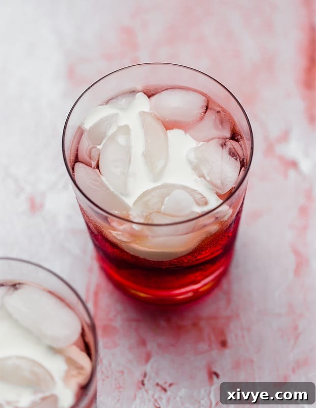 Heavy cream settling into a glass cup full of Italian cream soda ingredients, unstirred, showcasing the beautiful layered effect before mixing.