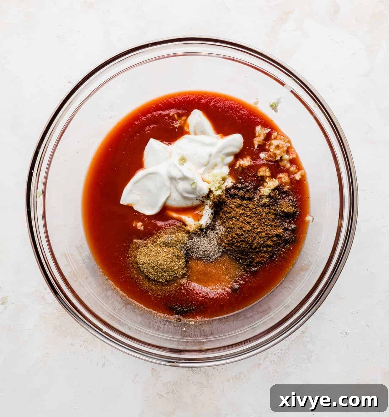A glass bowl with tomato sauce, Greek yogurt, and seasonings for Butter chicken.
