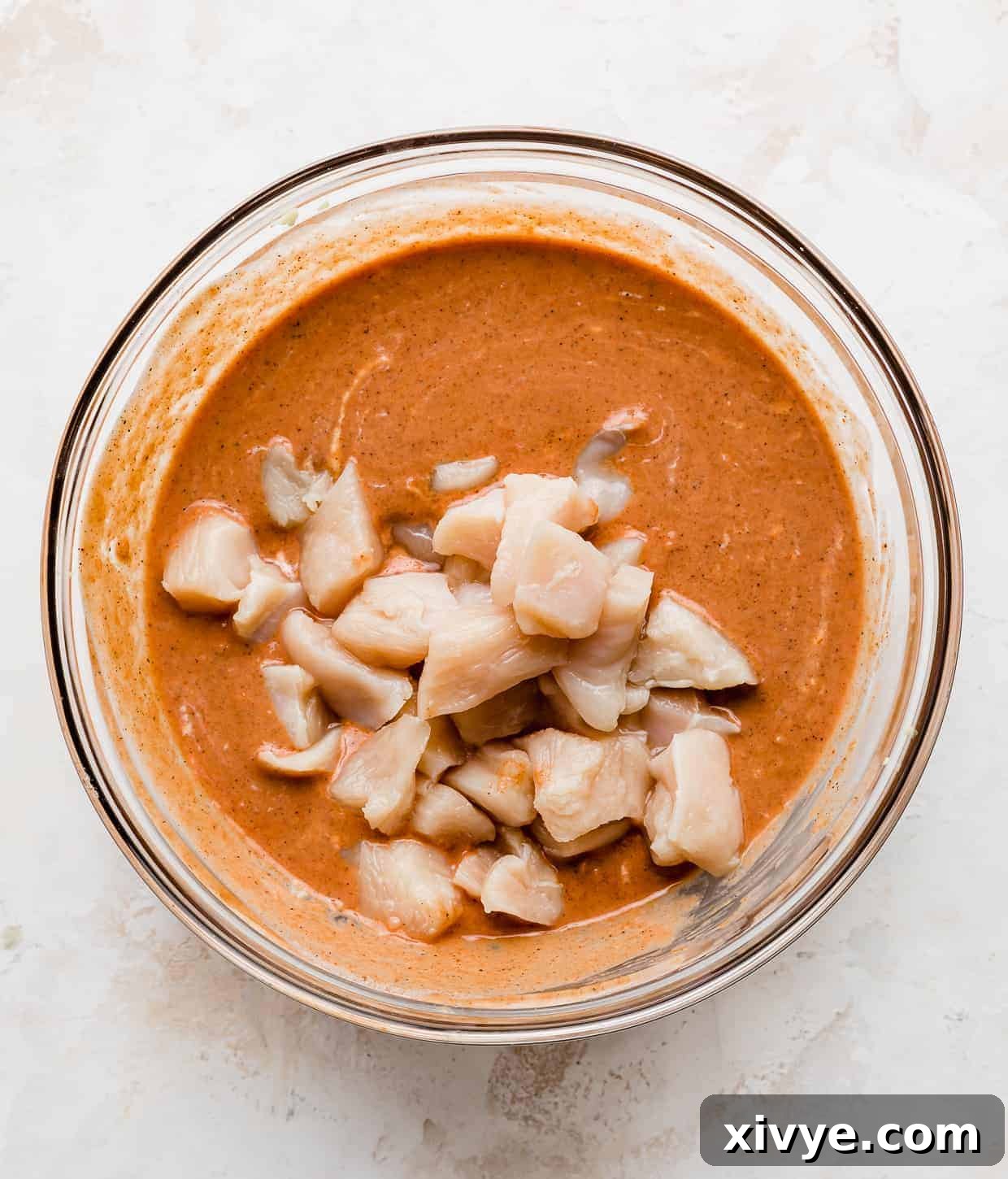 Raw cubed chicken in a orange butter chicken marinade.