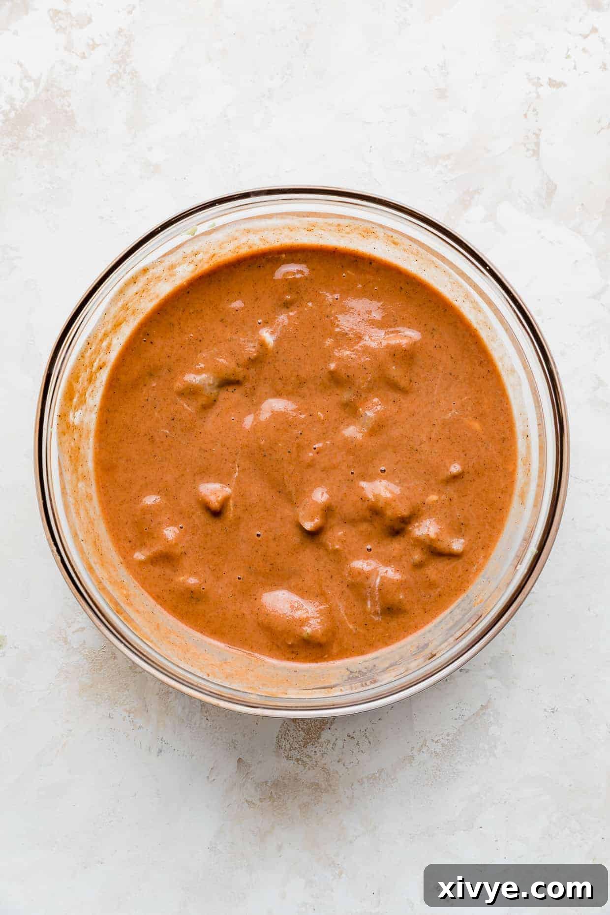 A red/orange marinade with cubed chicken in it.