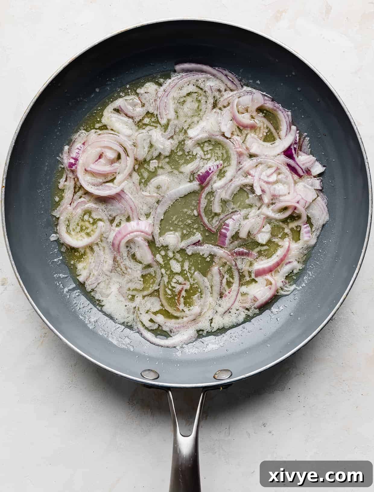 A skillet with butter and sliced red onion in it.