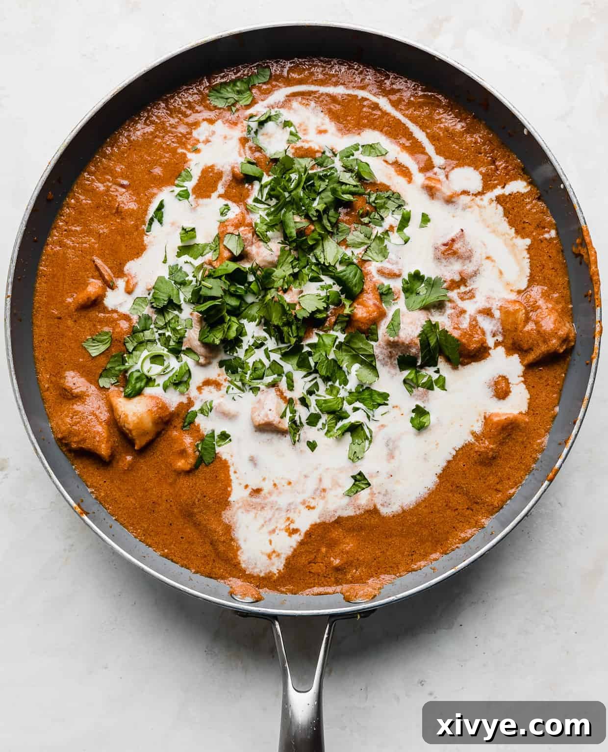 A skillet with Indian Butter Chicken in it with heavy cream and cilantro overtop.