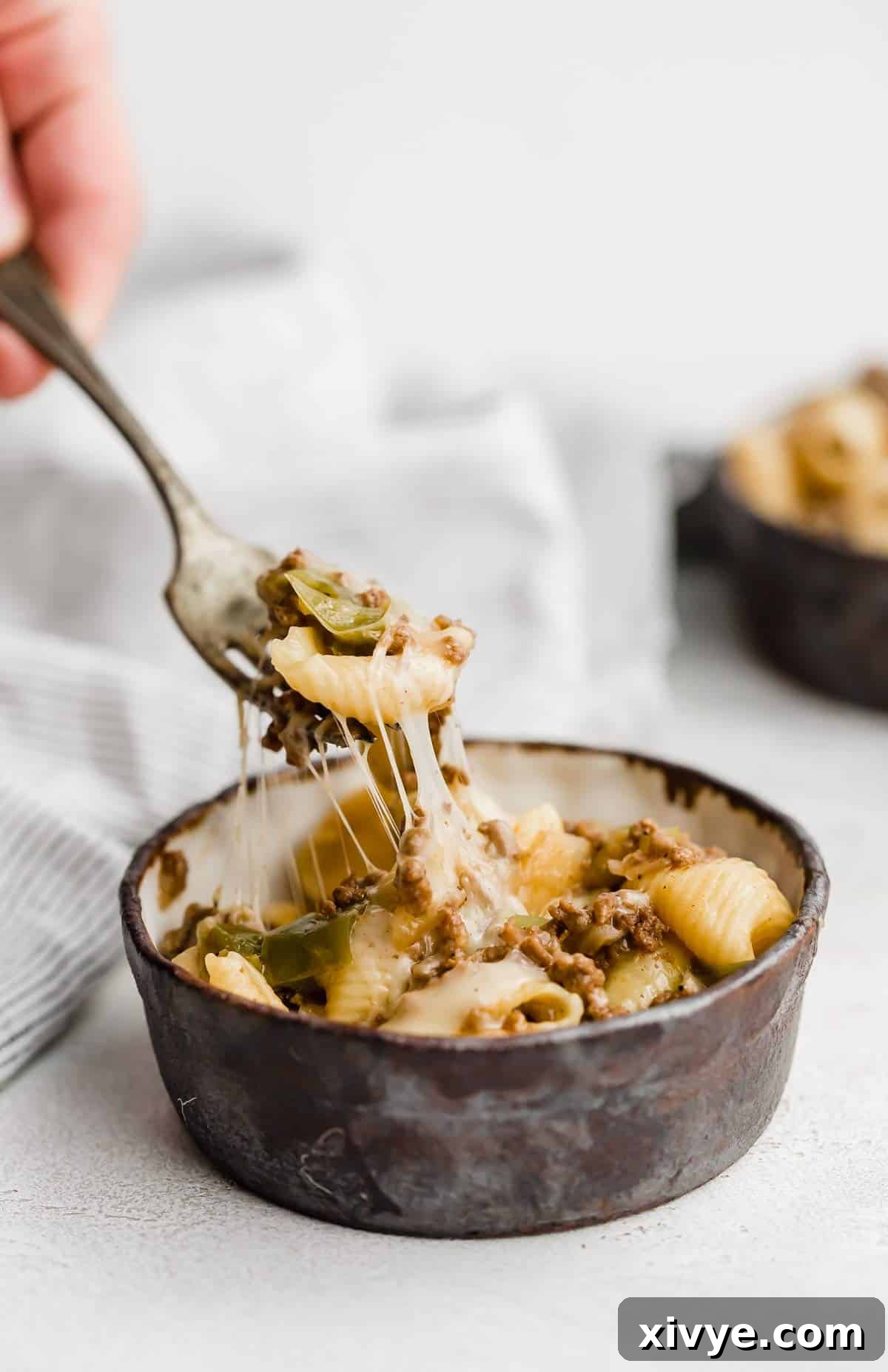 Creamy Instant Pot Philly Cheesesteak Pasta 5 A fork picking up Instant Pot Philly Cheesesteak Pasta from a black bowl on a white background, highlighting the creamy texture and melted cheese.