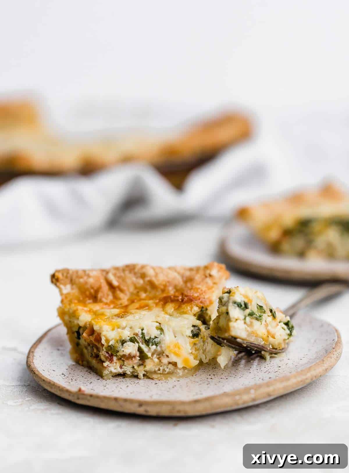 Spinach and Bacon Quiche on a beige plate with a fork next to the pie slice.