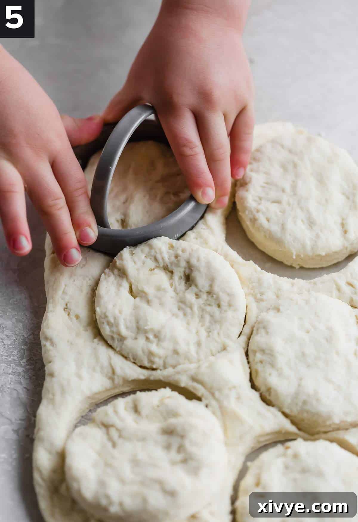 Small hands using a biscuit cutter to cut round biscuits from dough, showing proper technique.