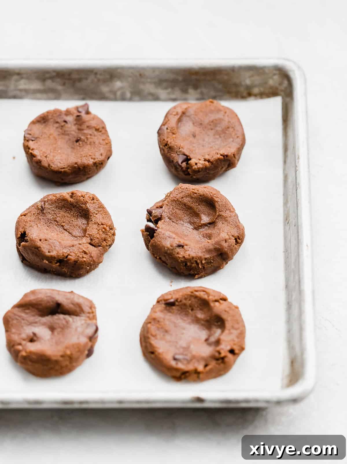 Nutella cookie dough portioned into round blobs on a baking sheet, half with indentations for stuffing.