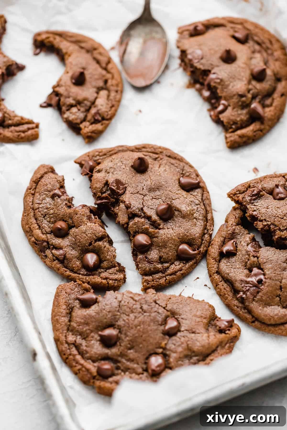 A baked Nutella Stuffed Nutella Cookie ripped in half on a white parchment lined baking sheet, showcasing the perfectly melted Nutella oozing from the center.