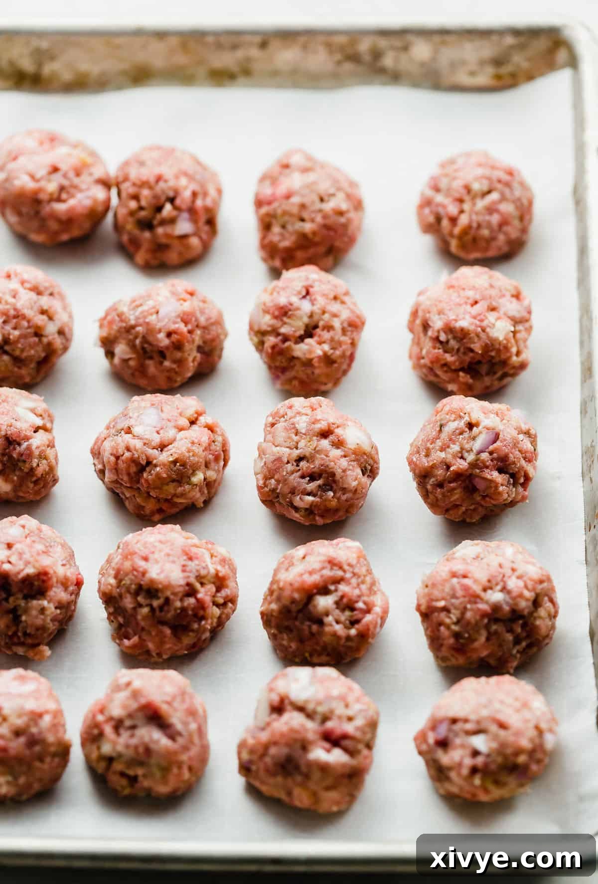 Raw Swedish Meatballs lined up in straight rows on a parchment lined baking sheet.