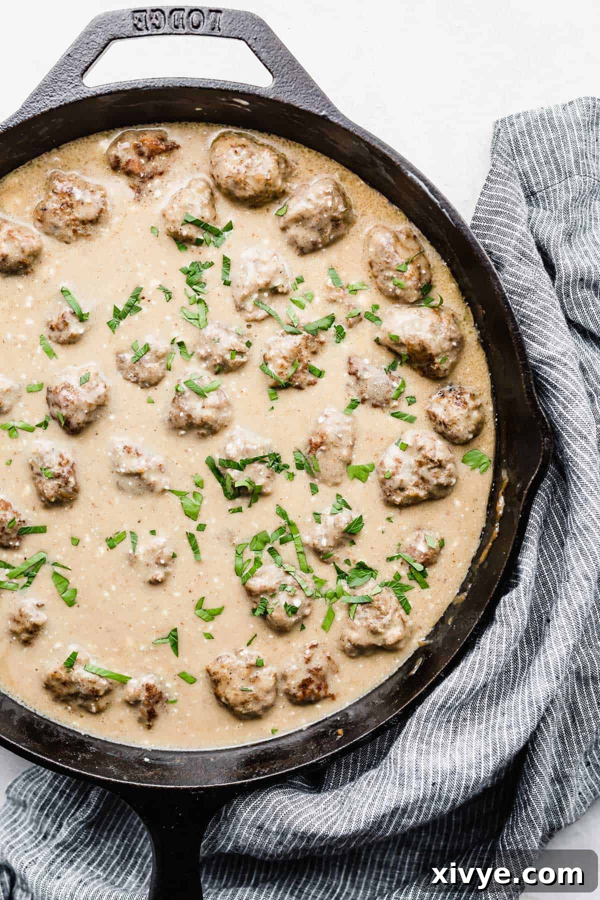 A skillet full of Swedish Meatballs and tan colored sauce on a white background.