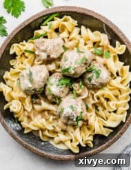 A black plate full of cooked egg noodles and Swedish Meatballs on top.