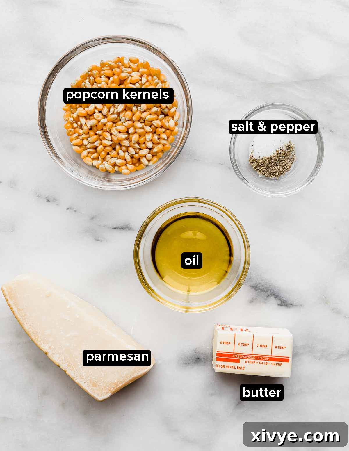 Gourmet Parmesan Popcorn 3 Parmesan Popcorn ingredients laid out on a white background: butter, oil, popcorn kernels, and a block of parmesan cheese.