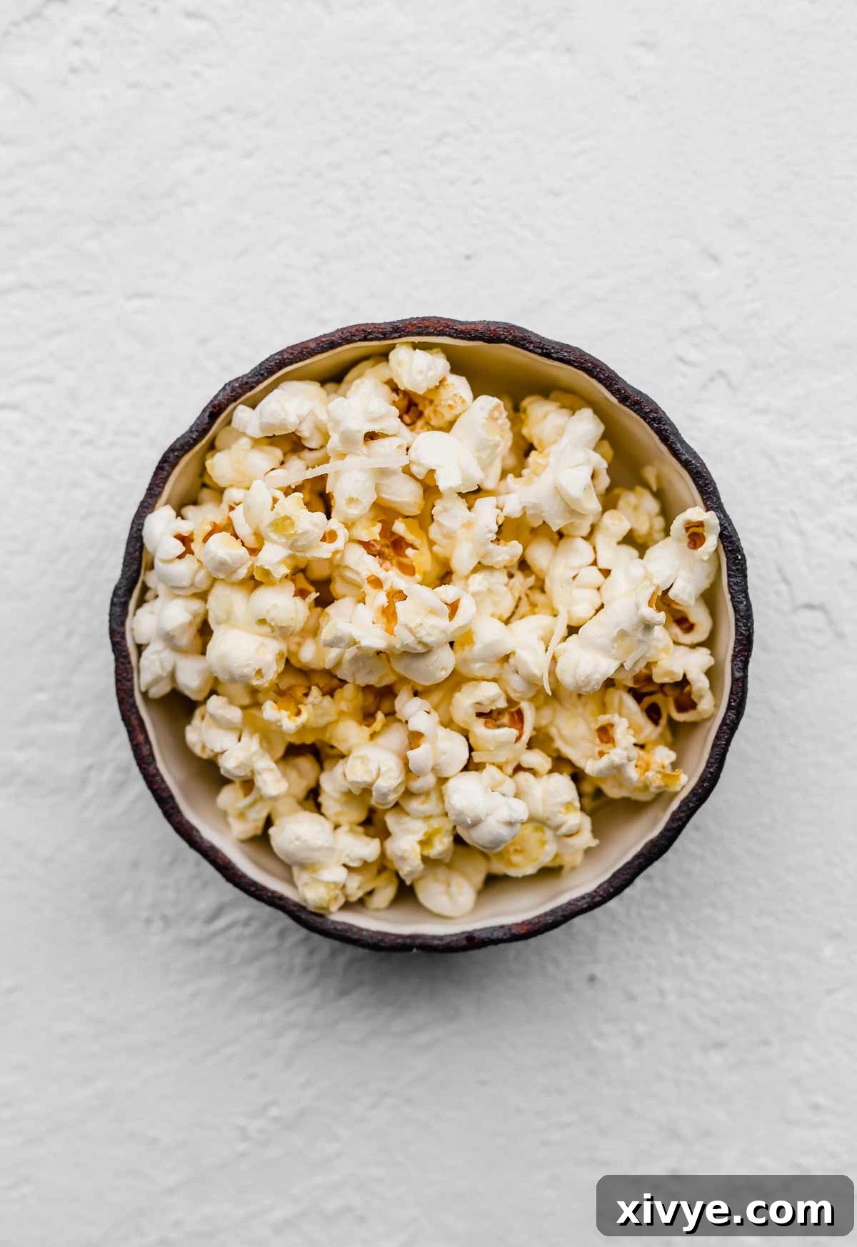 Gourmet Parmesan Popcorn 4 Parmesan Popcorn served in a black bowl on a white textured background, ready to be enjoyed.
