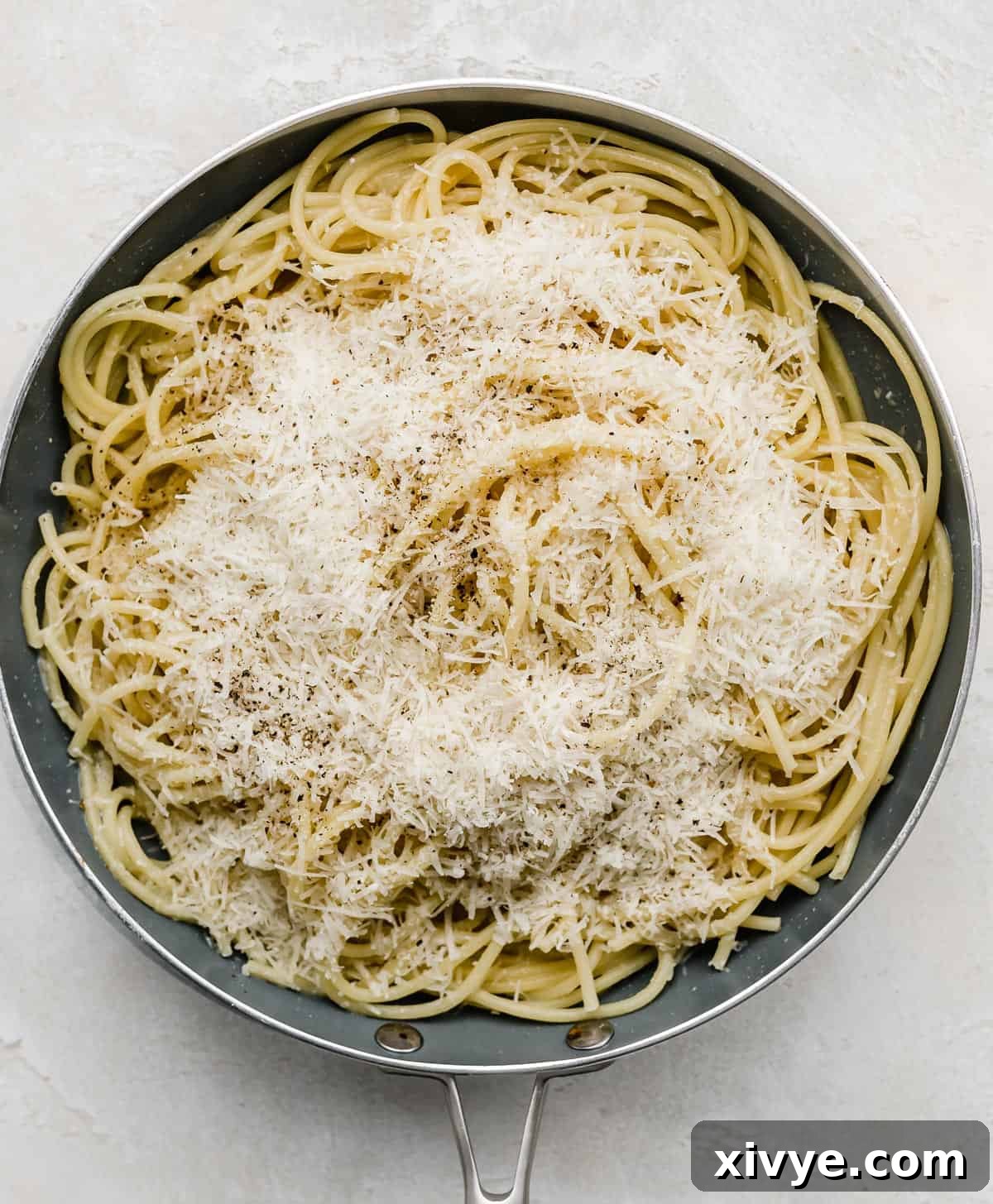 The Ultimate Bucatini Cacio e Pepe 4 A gray skillet full of bucatini noodles topped with fresh parmesan cheese.