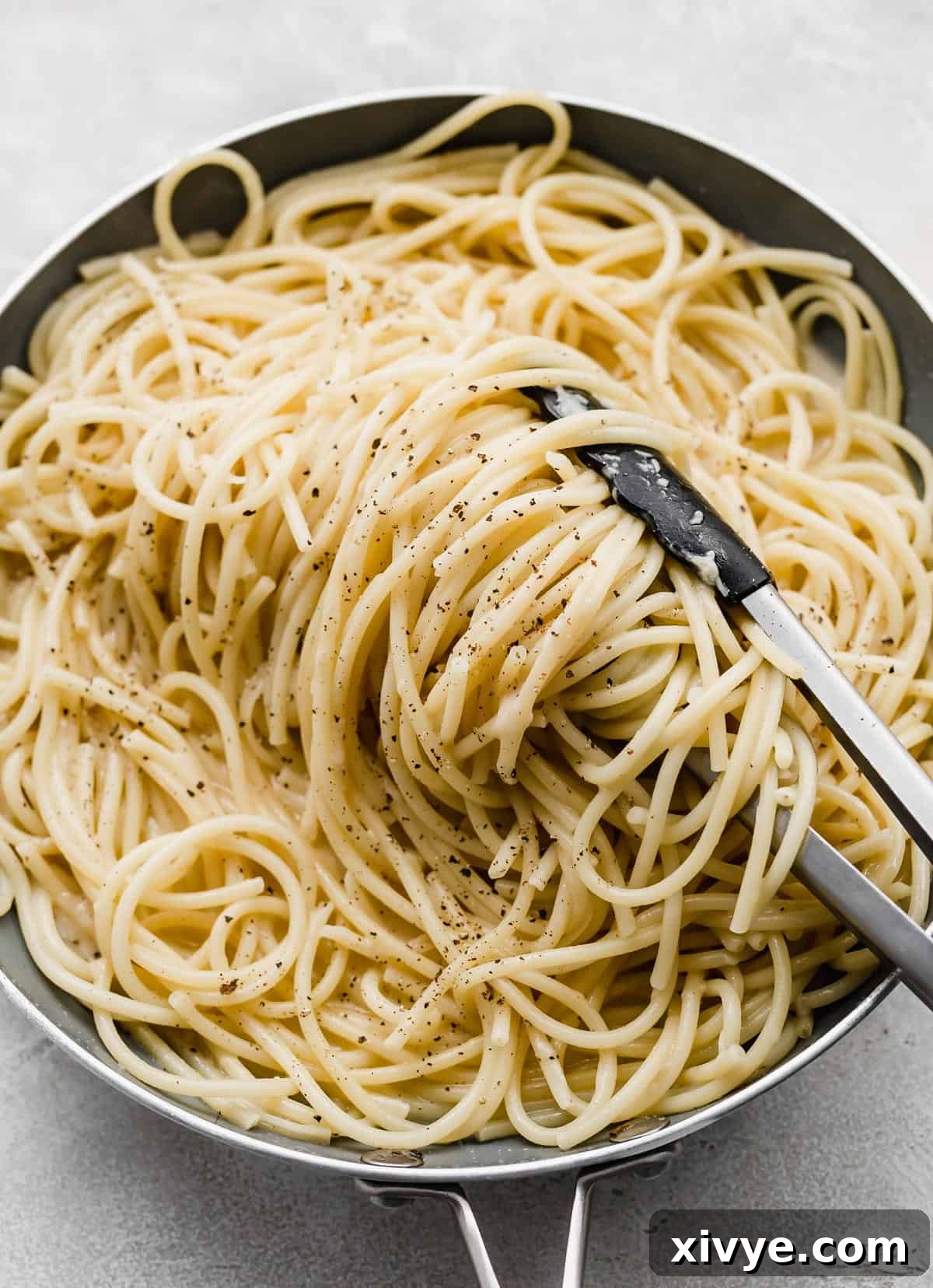 The Ultimate Bucatini Cacio e Pepe 5 Kitchen tongs turning Bucatini Cacio e Pepe noodles in a skillet.