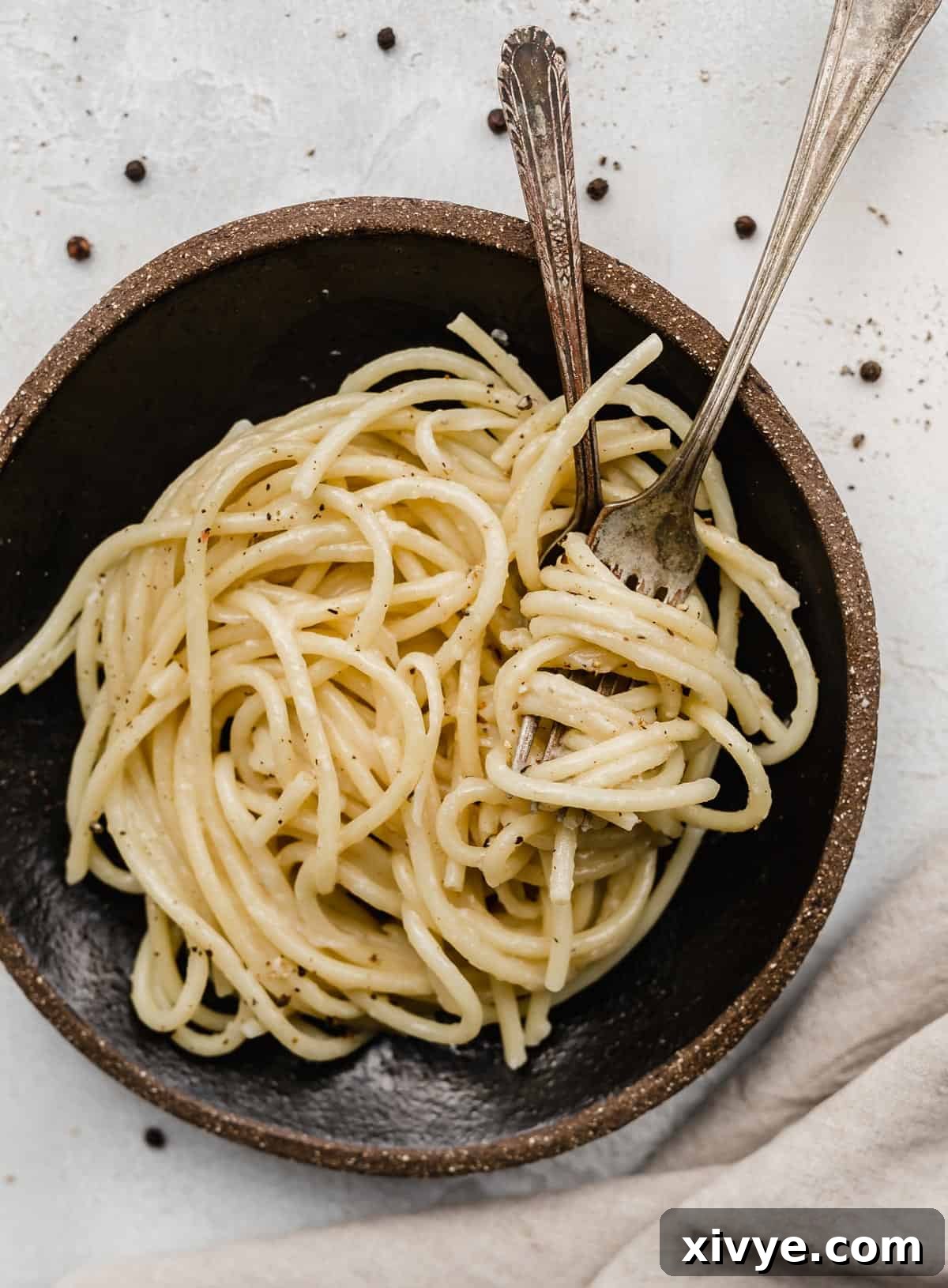 The Ultimate Bucatini Cacio e Pepe 6 A black plate with two forks twirled into Bucatini Cacio e Pepe noodles.