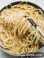 The Ultimate Bucatini Cacio e Pepe 7 Bucatini Cacio e Pepe noodles in a skillet pan with kitchen tongs turning the noodles over.