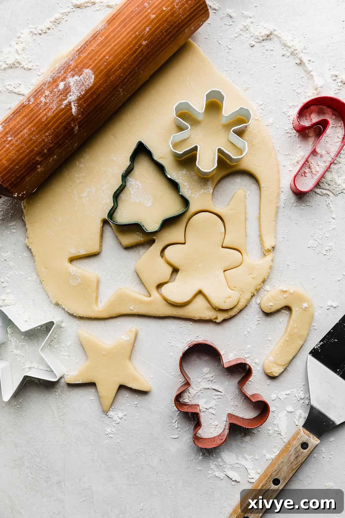 Sugar cookie dough rolled out on a gray background with cookie cutters cutting out the dough.