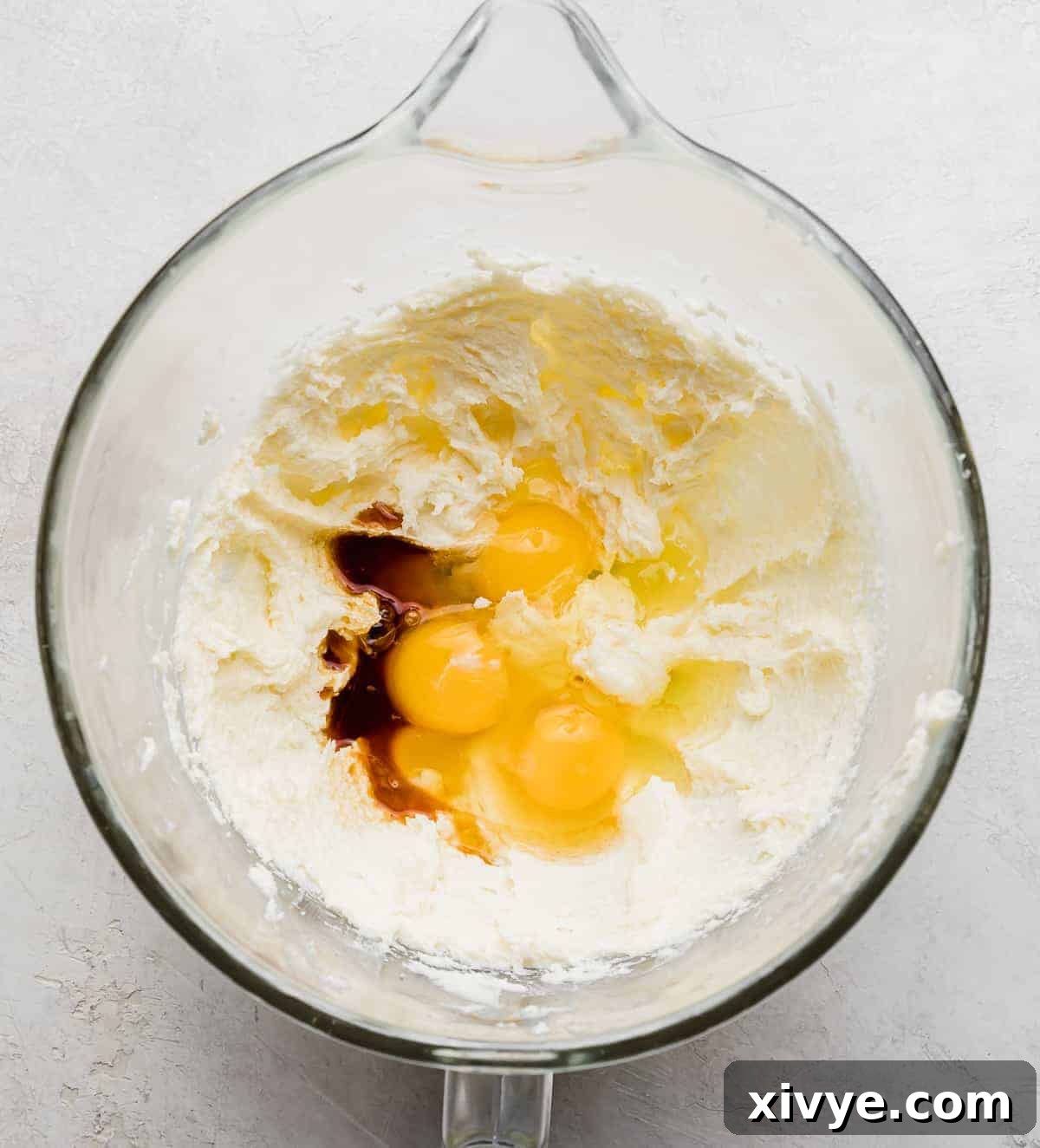 A glass bowl with creamed butter and sugar, eggs, and vanilla.