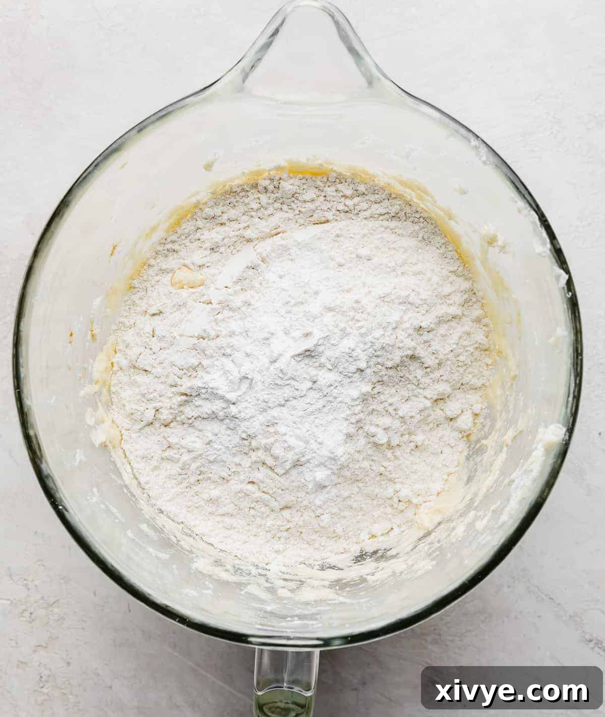 Flour and baking powder in a glass bowl on a gray background.
