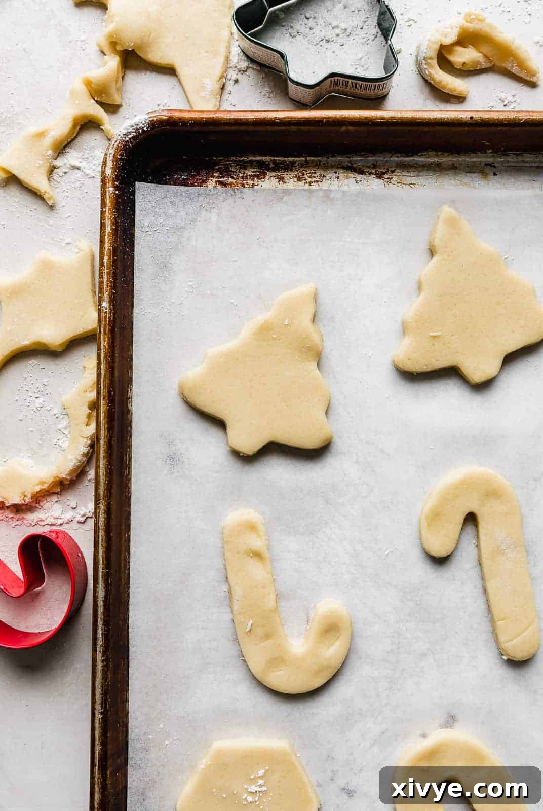 Sugar cookie dough cut into a tree and candy canes on a parchment lined baking sheet.