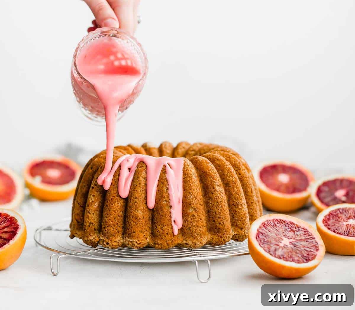 Blood Orange Glaze being drizzled generously over a blood orange cardamom bundt cake, creating beautiful pink rivulets.