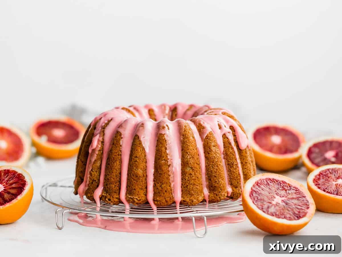 A close-up of vibrant pink glaze flowing down a blood orange bundt cake on a clean white background.