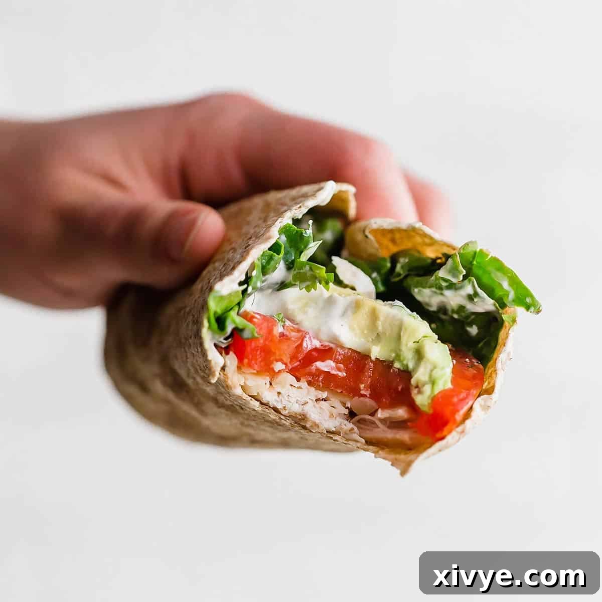 Lean and Green Chicken Wraps 6 A hand holding a Healthy Chicken Wrap with a bite taken out of the wrap showing the avocado, tomato, chicken, and spinach in the wrap.