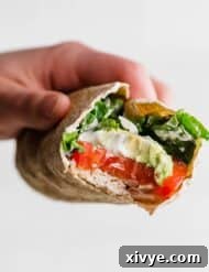 Lean and Green Chicken Wraps 7 A hand holding a Healthy Chicken Wrap with a bite taken out of the wrap showing the avocado, tomato, chicken, and spinach in the wrap.