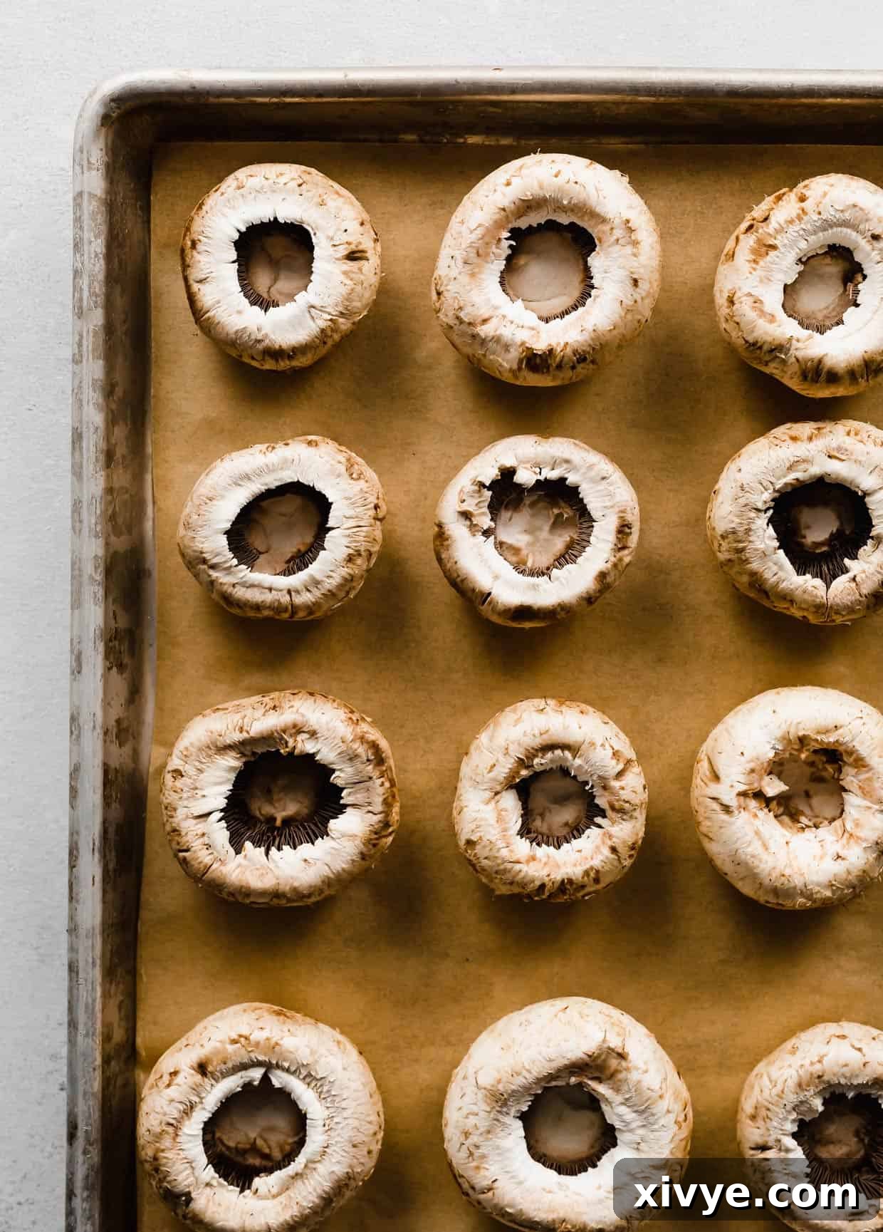 Zesty Italian Sausage Stuffed Mushrooms 4 White mushrooms on a parchment lined baking sheet, gill sides up.