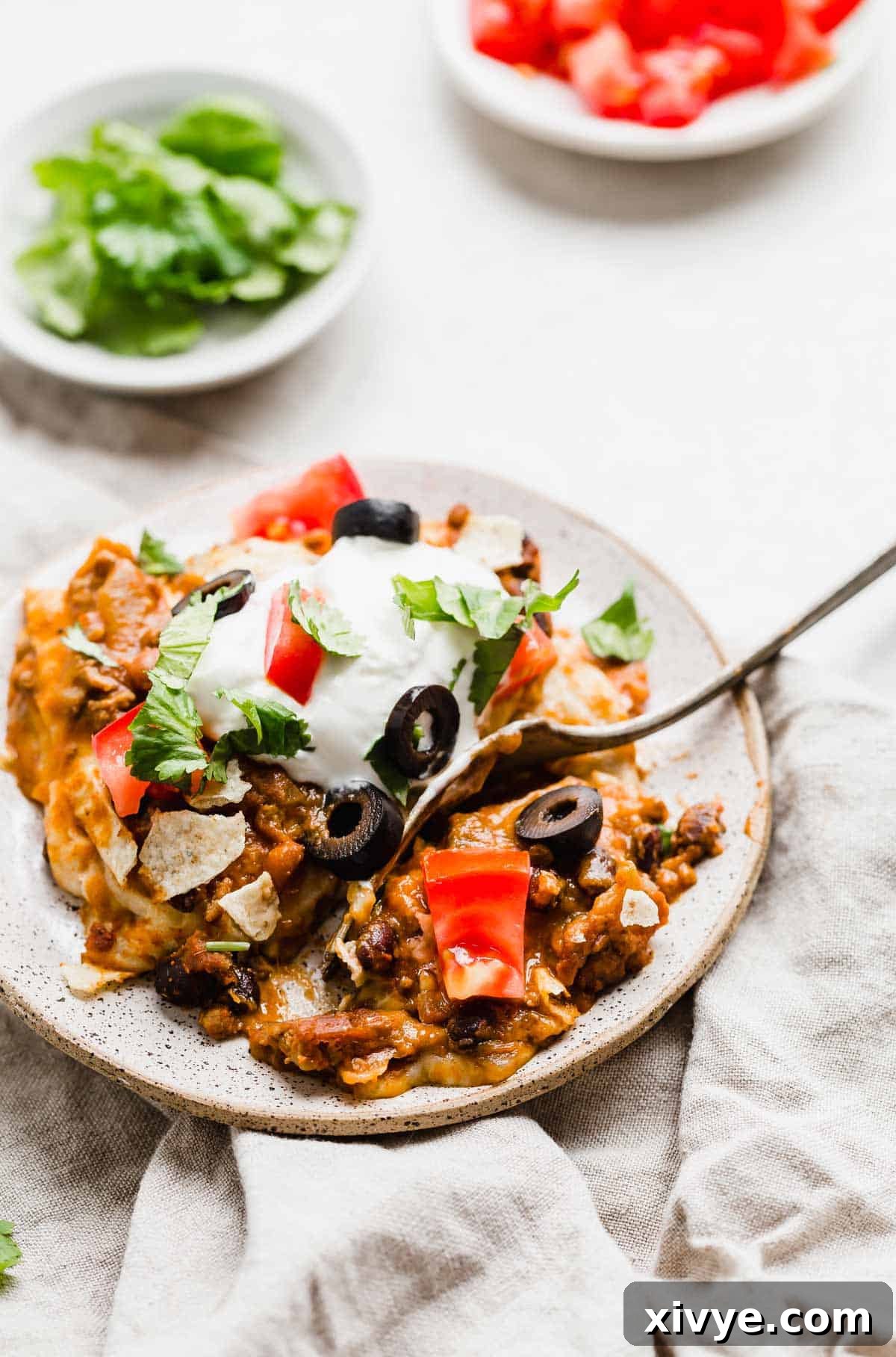 Mexican Lasagna topped with olive slices, sour cream, and shredded lettuce, on a white plate.